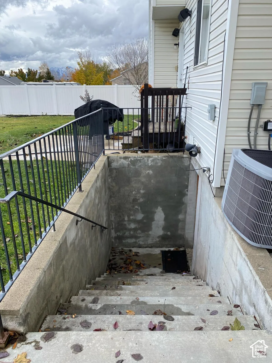 Exterior concrete stairwell with metal handrails, white vinyl siding, and white vinyl perimeter fencing