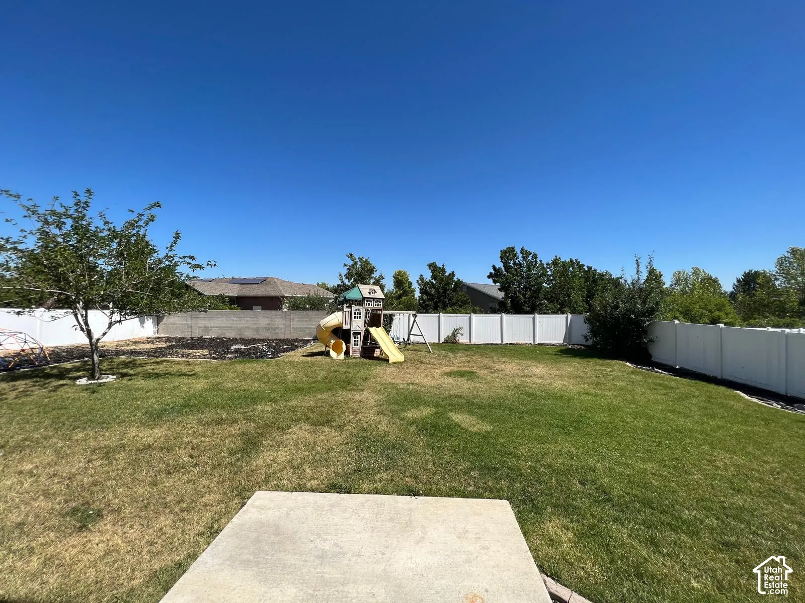 Expansive backyard featuring a concrete patio, perimeter vinyl fencing, and mature trees
