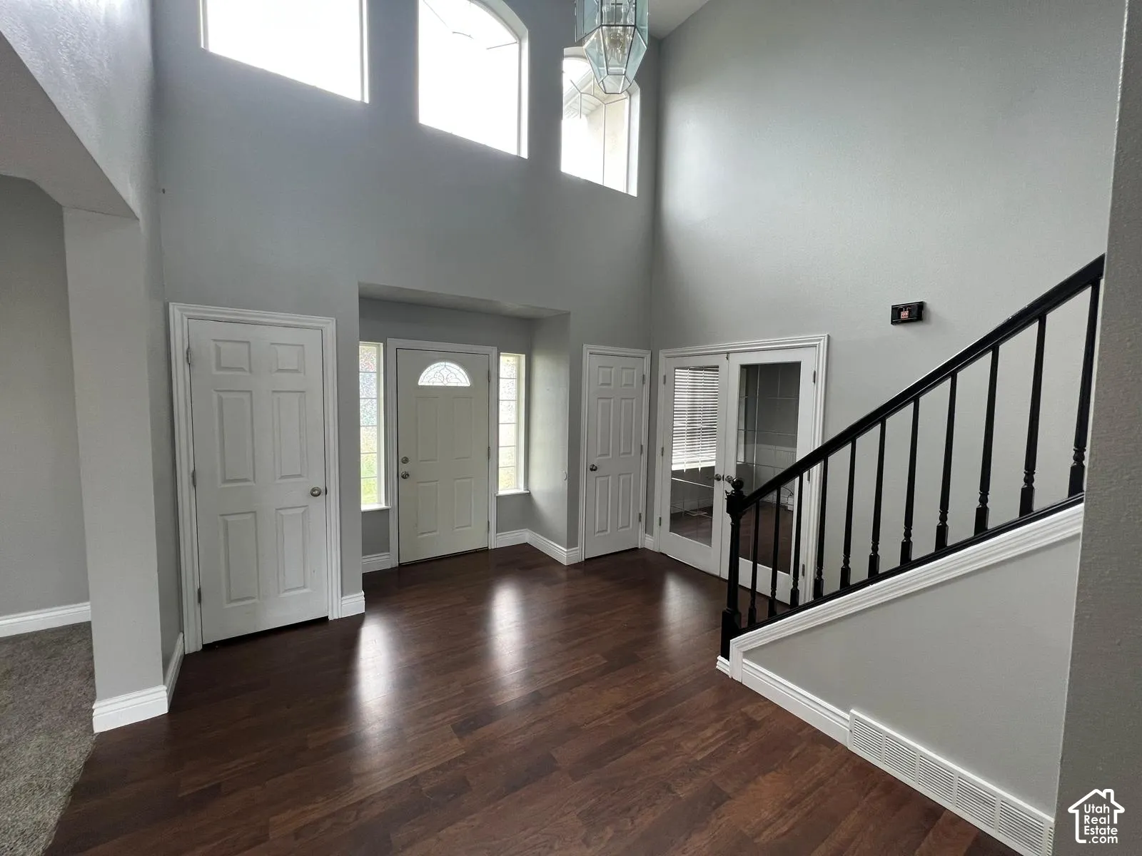 Foyer featuring a vaulted ceiling, wood-finish flooring, multi-pane transom windows, staircase with black balusters, and a glass-paneled entry door