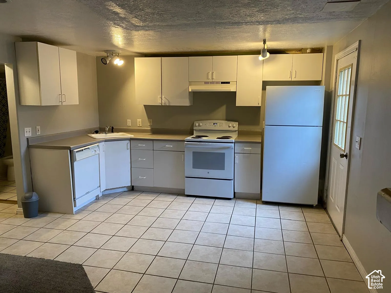 Kitchen featuring white cabinetry, solid-surface countertops, integrated dishwasher, white range, and ceramic tile flooring