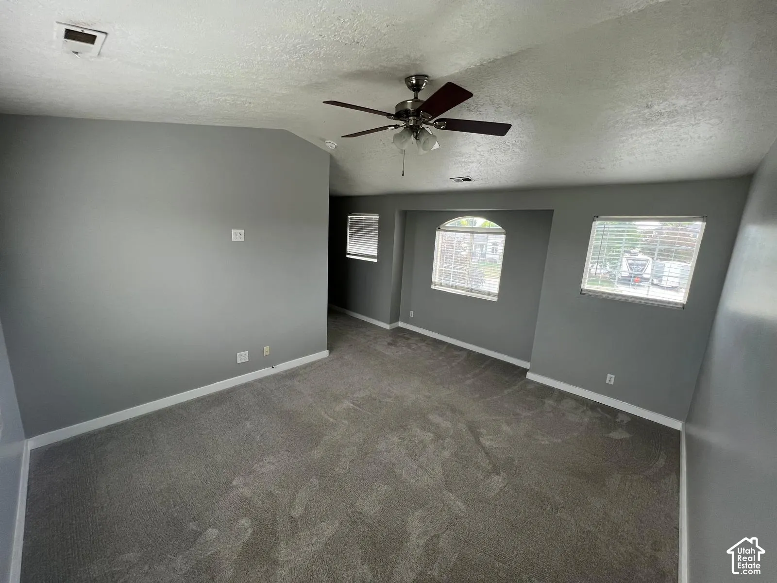 Vaulted ceilings featuring a central overhead fan, neutral wall finishes, carpeted flooring, and a recessed window nook with an arched detail