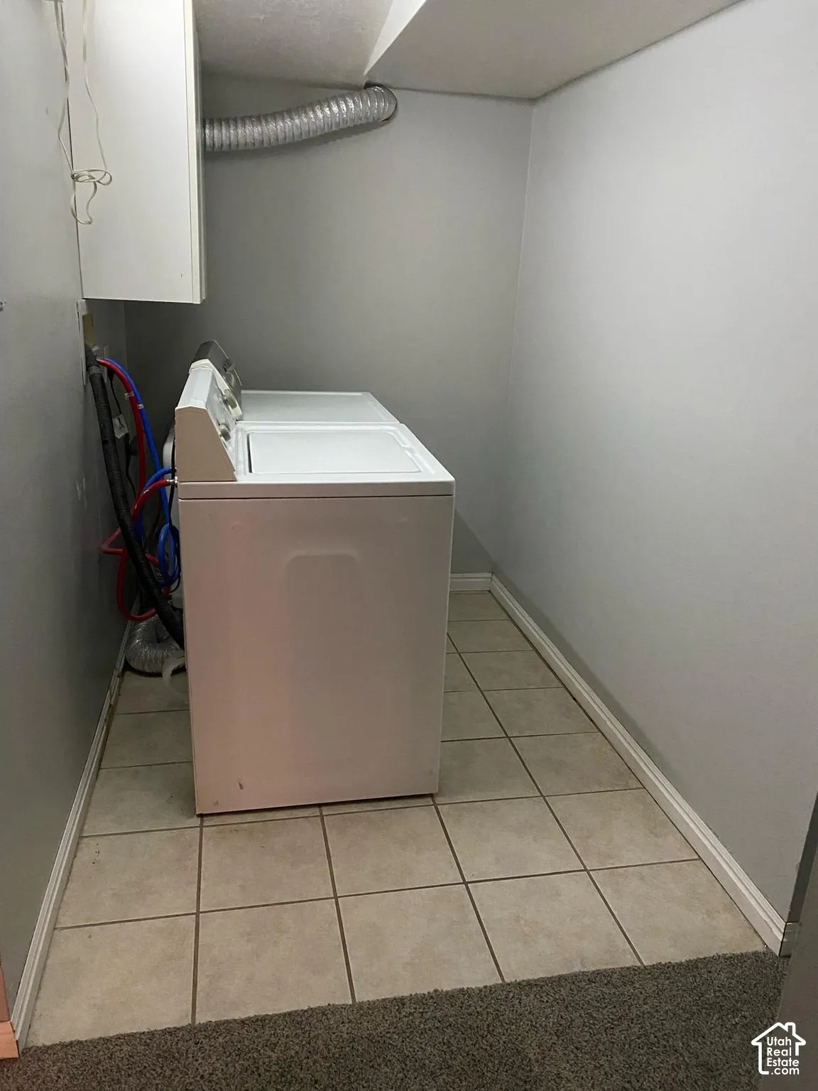 Utility area featuring neutral ceramic tile flooring and white wall-mounted cabinetry