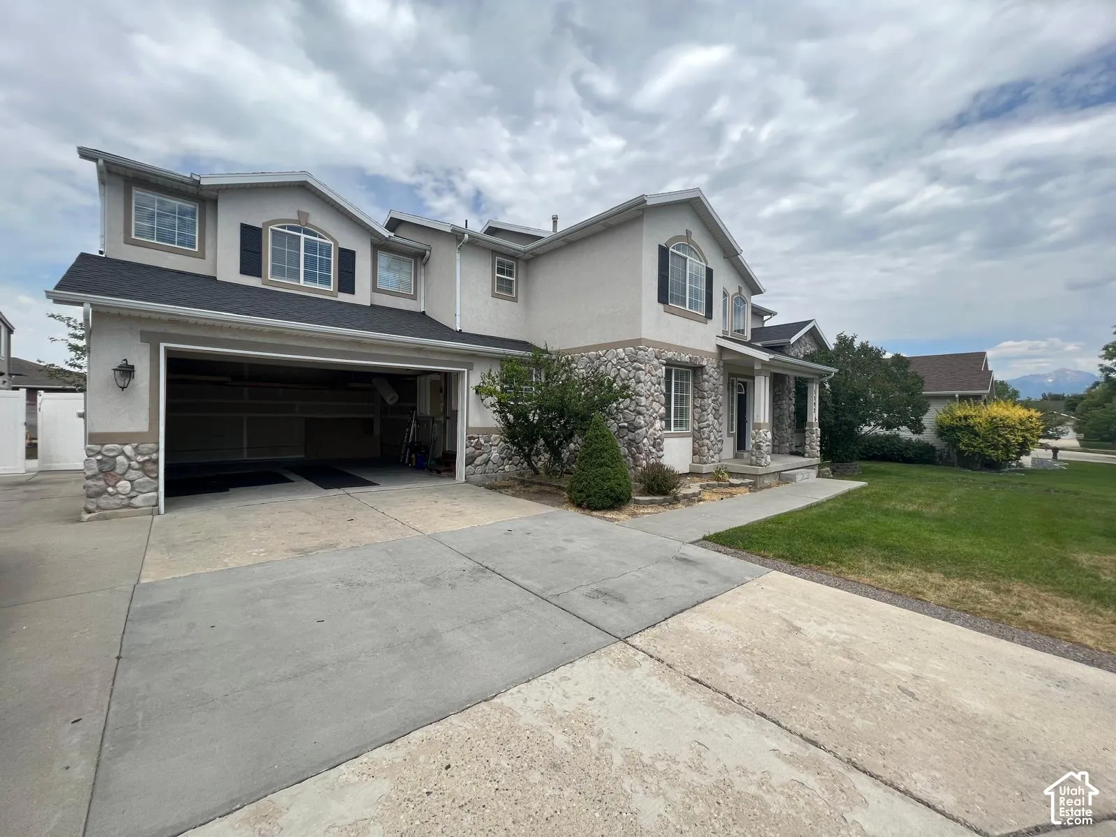 Multi-level exterior featuring stone veneer accents, stucco siding, arched window detailing, and a three-car garage