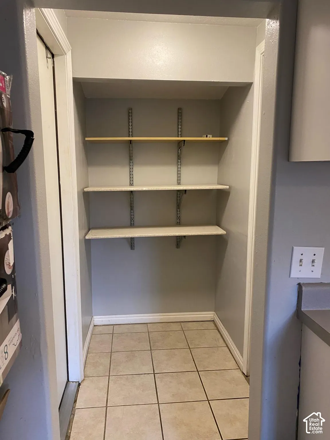 Built-in storage area featuring three adjustable open shelves with a wall-mounted track system and tiled flooring