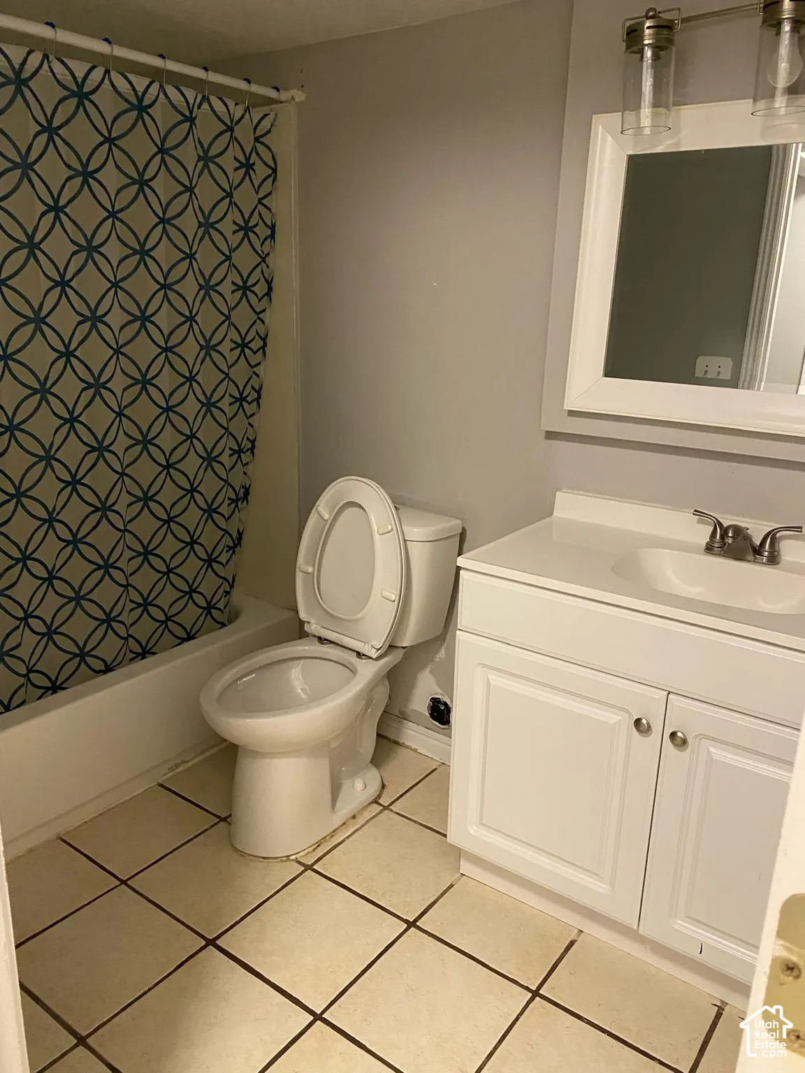 Bathroom featuring a white vanity cabinet with an integrated sink, brushed-nickel faucet hardware, wall-mounted light fixture, square-tiled flooring, and a porcelain-enamel bathtub
