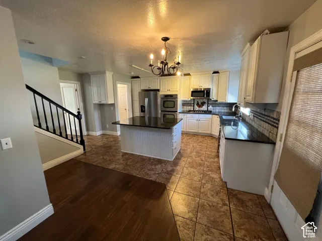 Kitchen featuring white cabinetry, center island with dark stone countertop, built-in stainless steel double wall oven, patterned tile flooring, and wood-finish flooring