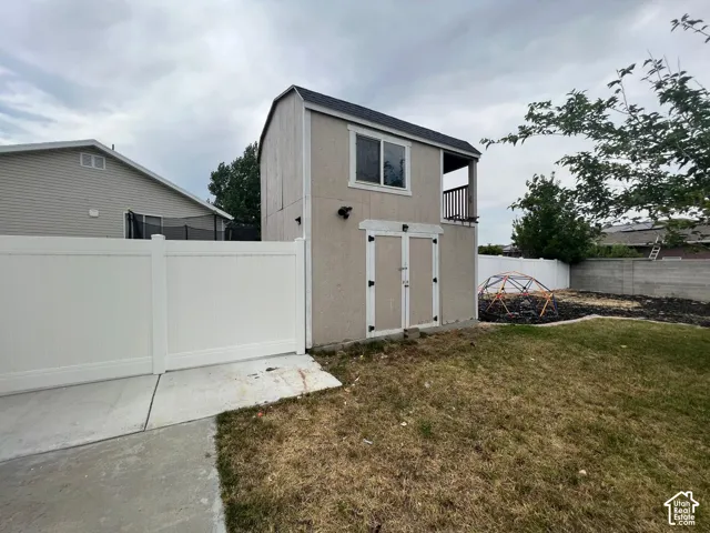 Two-story exterior storage structure featuring a balcony, double-door access, a vinyl fence, and a concrete pad
