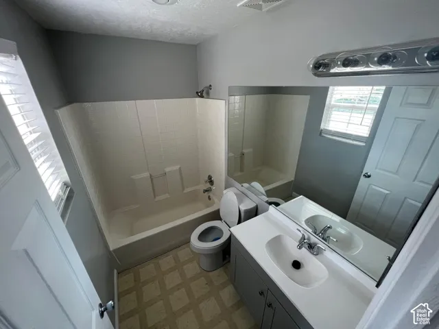 Bathroom featuring a tub-shower combination with tiled surround, a vanity with a white countertop and integrated sink, a large wall-mounted mirror, and tile flooring