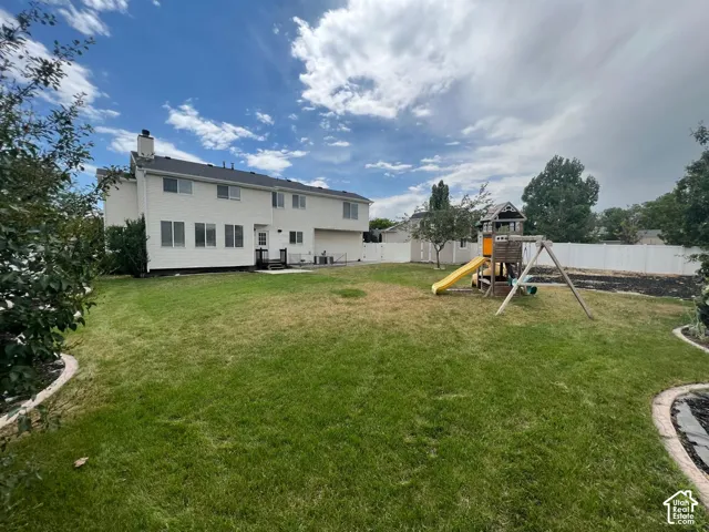Spacious backyard featuring a large grass lawn, white perimeter fencing, and mature trees