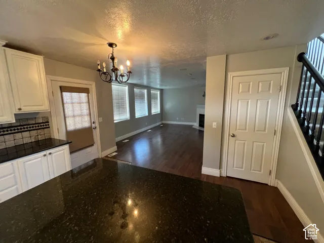 Kitchen featuring dark stone countertops, shaker-style cabinetry, a multi-arm chandelier, and wood-finish flooring