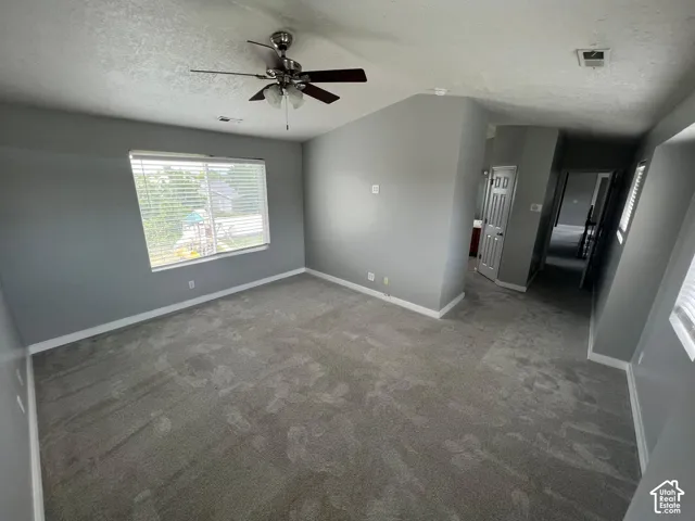 Vaulted ceilings, neutral wall color, wall-to-wall carpeting, ceiling fan with light fixture, and windows with horizontal blinds
