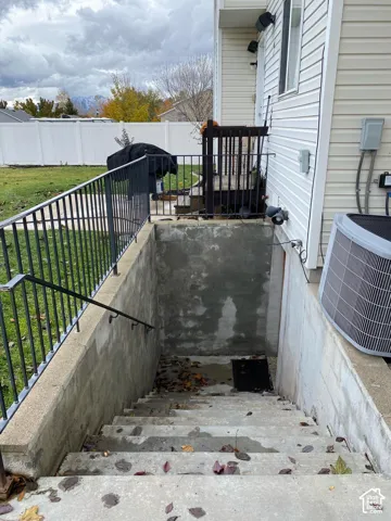 Exterior concrete stairwell with metal handrails, white vinyl siding, and white vinyl perimeter fencing
