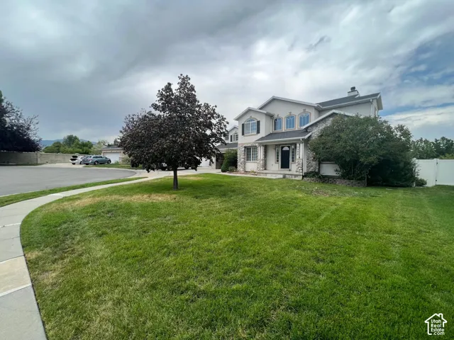 Two-story residence featuring light-toned exterior cladding, multi-textured stone veneer, arched window detailing, and a multi-gabled roofline, situated on a corner lot with an established lawn