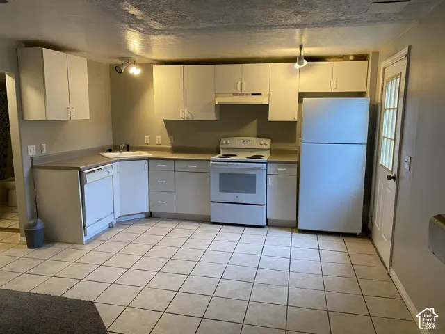 Kitchen featuring white cabinetry, solid-surface countertops, integrated dishwasher, white range, and ceramic tile flooring