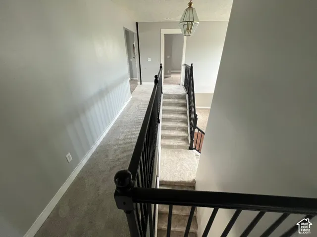 Hallway featuring wall-to-wall carpeting, metal stair railings with vertical balusters, and a geometric pendant light fixture
