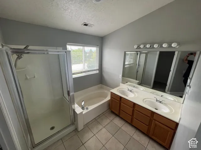 Bathroom featuring a dual-sink vanity with a large wall-mounted mirror, a soaking tub, and a separate glass-enclosed shower with tile flooring