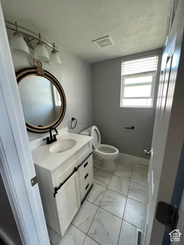 White vanity with a solid-surface countertop, matte black faucet, triple-light vanity fixture, and tiled flooring