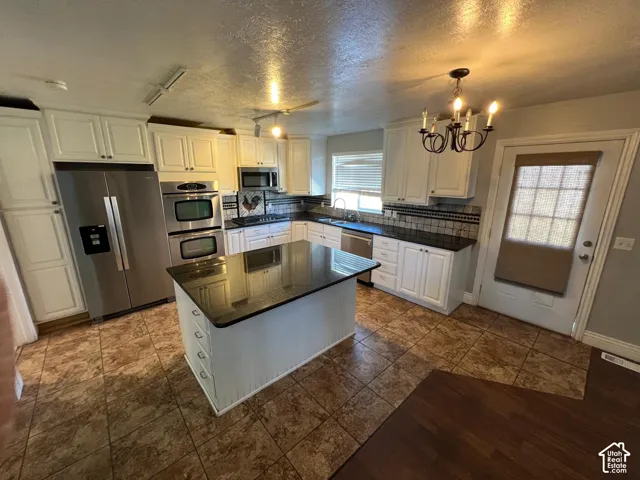 Kitchen featuring white cabinetry, an island with a black countertop, stainless steel appliances, a built-in double oven, and tile flooring
