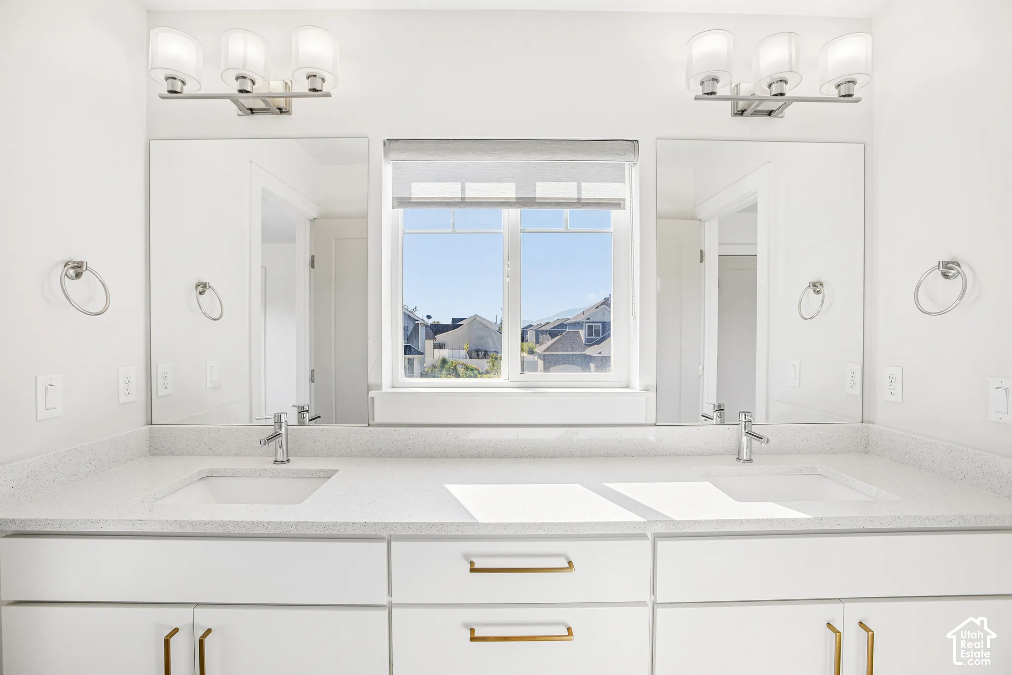 Double vanity featuring white cabinetry, brass-tone hardware, a solid-surface countertop with dual undermount sinks, wall-mounted light fixtures, and two rectangular mirrors