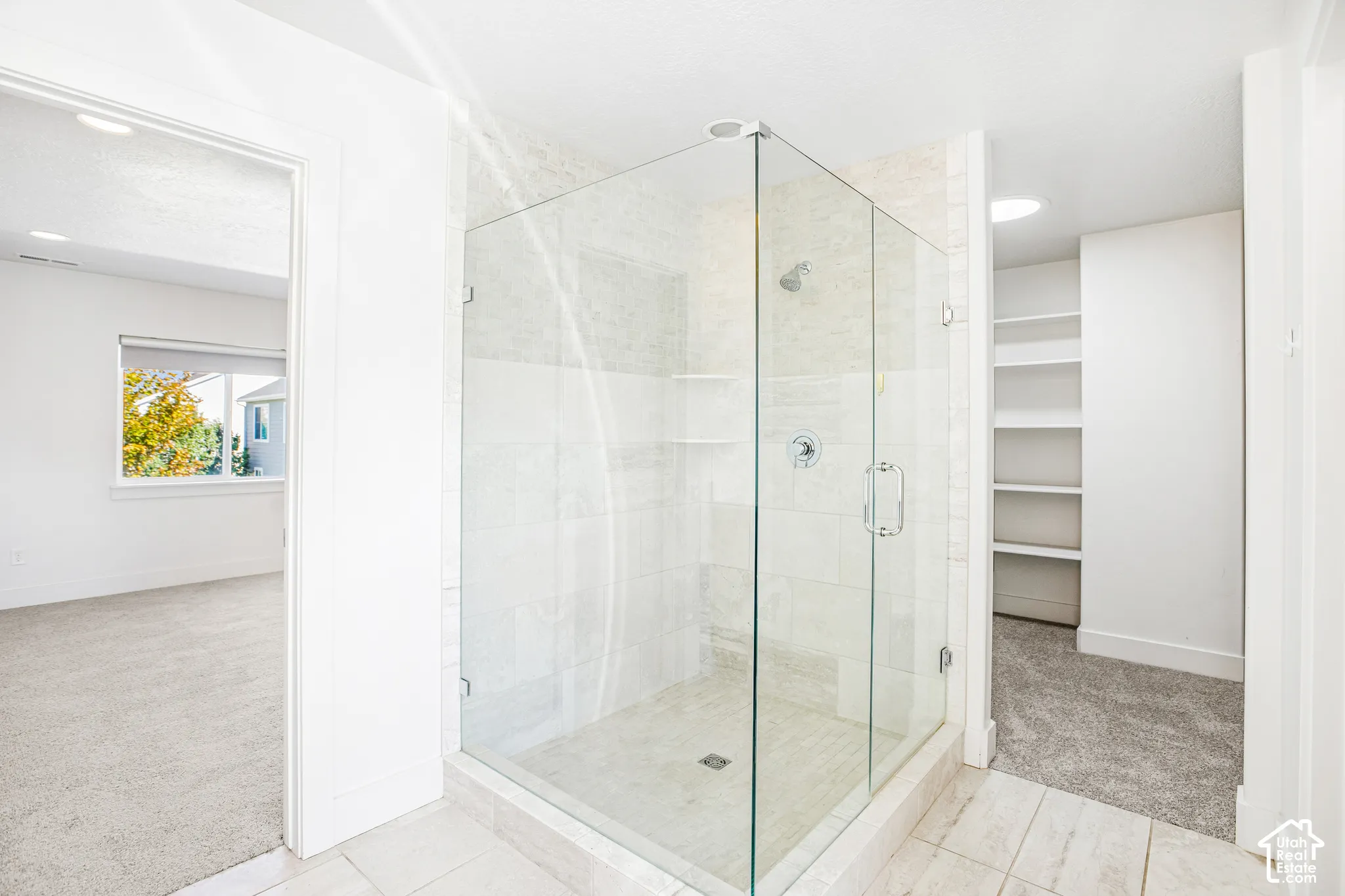 Walk-in shower featuring a glass enclosure, wall-mounted shower head, built-in shelving, and large-format tile wall surrounds, accompanied by built-in shelving units