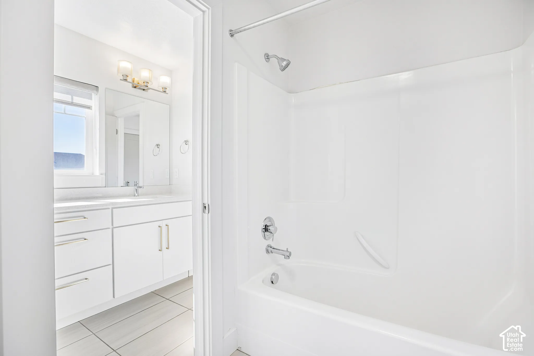 Bathroom featuring a white vanity with integrated basin, polished chrome fixtures, white tub-and-shower combination, and tile flooring