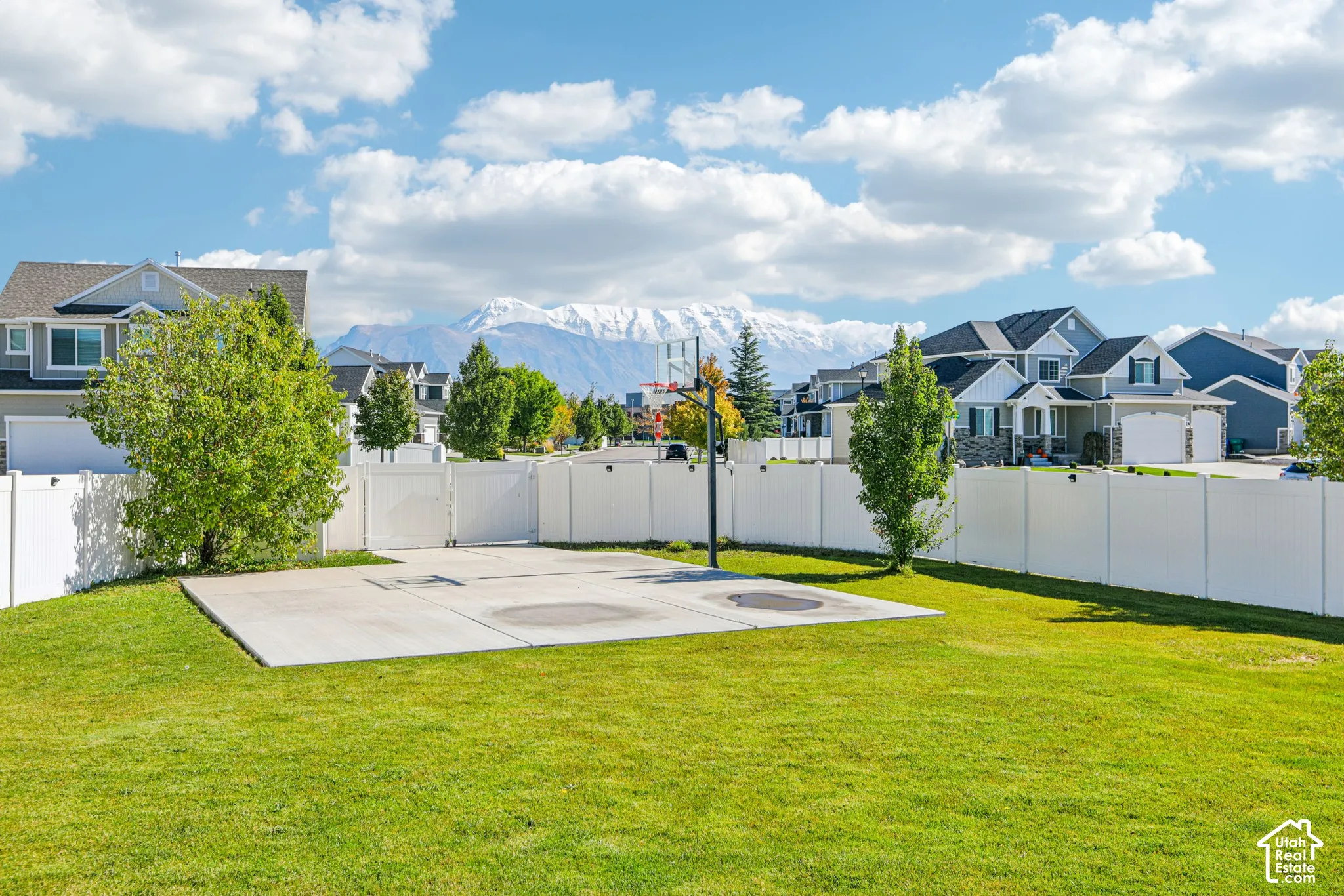 Backyard featuring a concrete sports court, basketball hoop, white vinyl privacy fencing, and mountain backdrop
