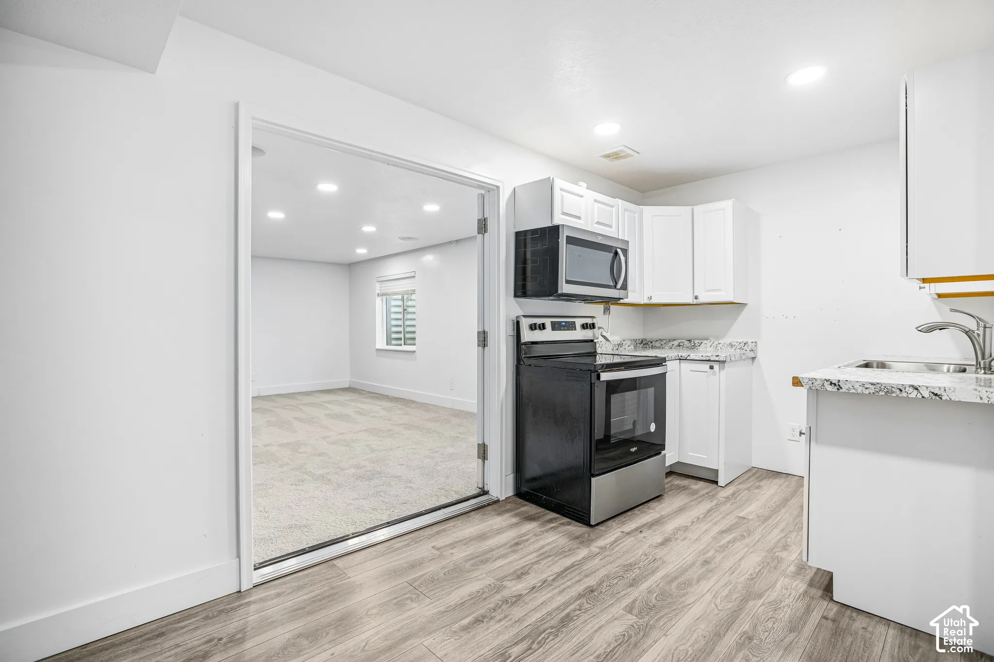 Kitchen featuring white cabinetry, stone-look countertops, stainless steel appliances, and wood-finish flooring, with double-door entry to a carpeted room