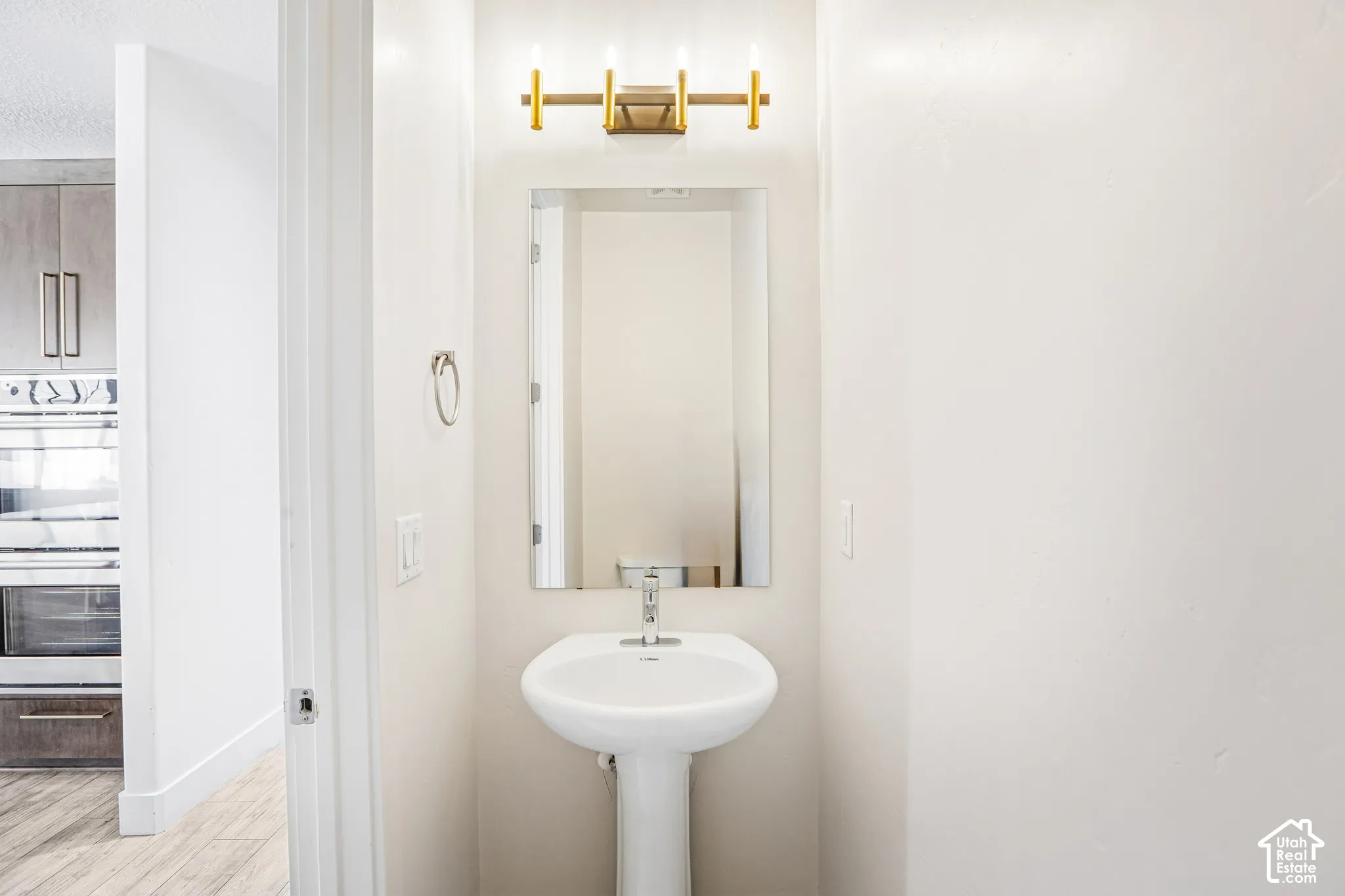 Pedestal sink with a single-handle faucet, rectangular frameless mirror, and a gold-tone four-light vanity fixture
