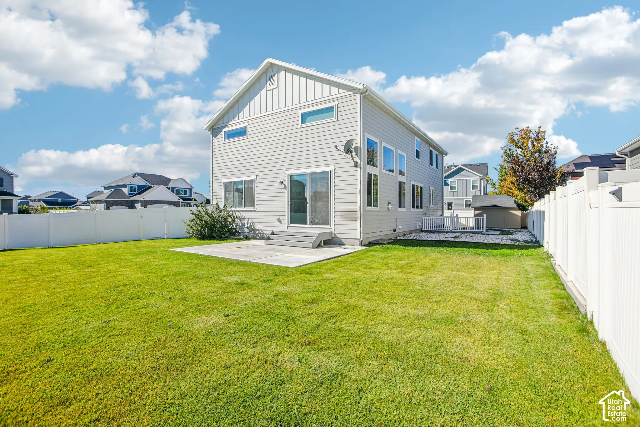 Expansive backyard featuring a manicured lawn, full-perimeter white vinyl fencing, and a concrete patio