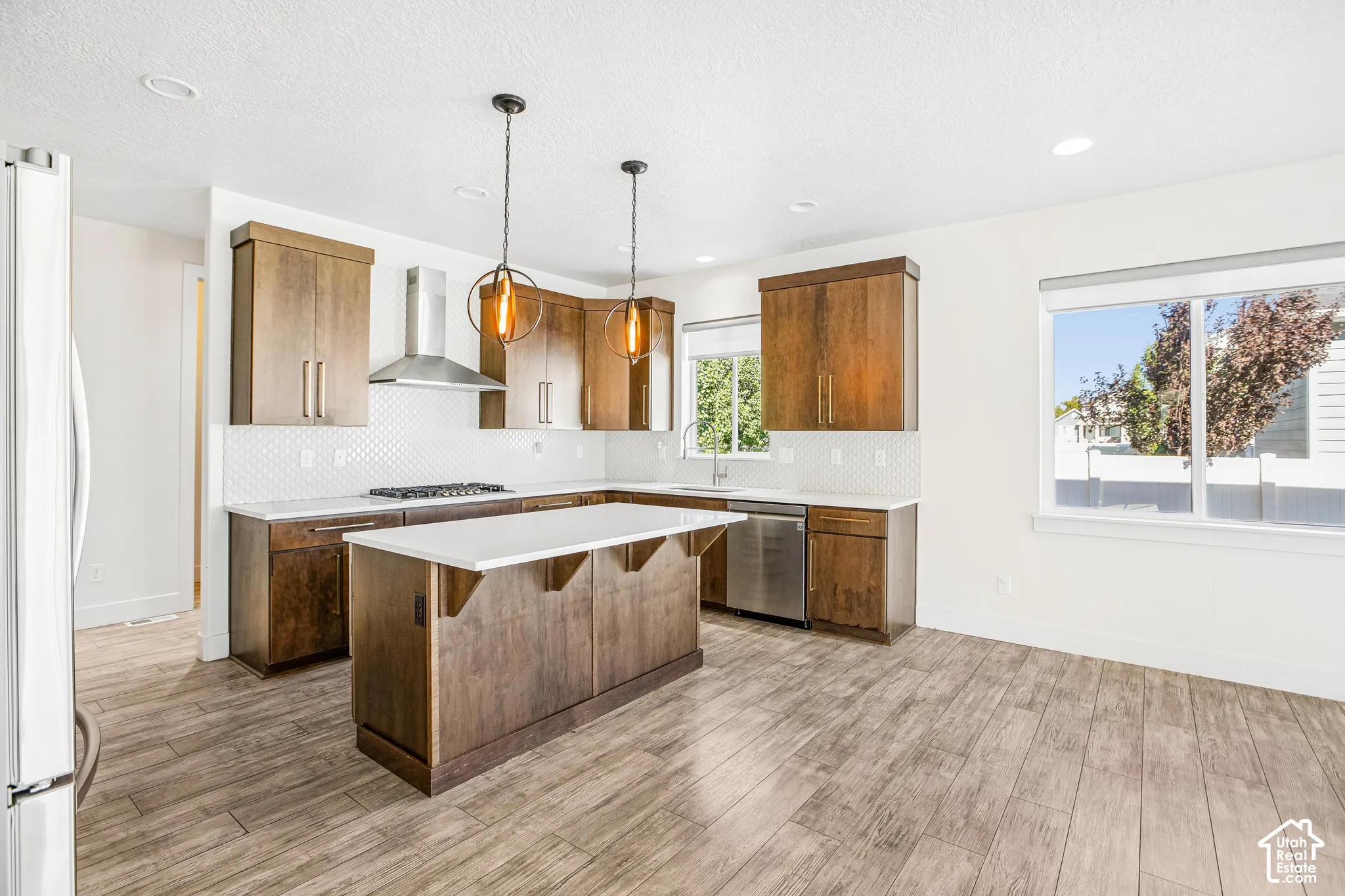 Kitchen featuring wood-finish cabinetry, a central island with quartz countertops, stainless steel appliances, a white hexagonal tile backsplash, and wood-finish flooring