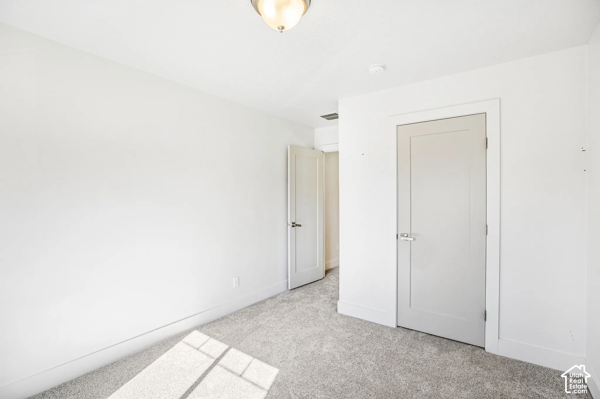 Room featuring neutral wall-to-wall carpeting, clean white wall finishes, and solid-core shaker-style interior doors with brushed nickel hardware, complemented by a flush-mount overhead light fixture