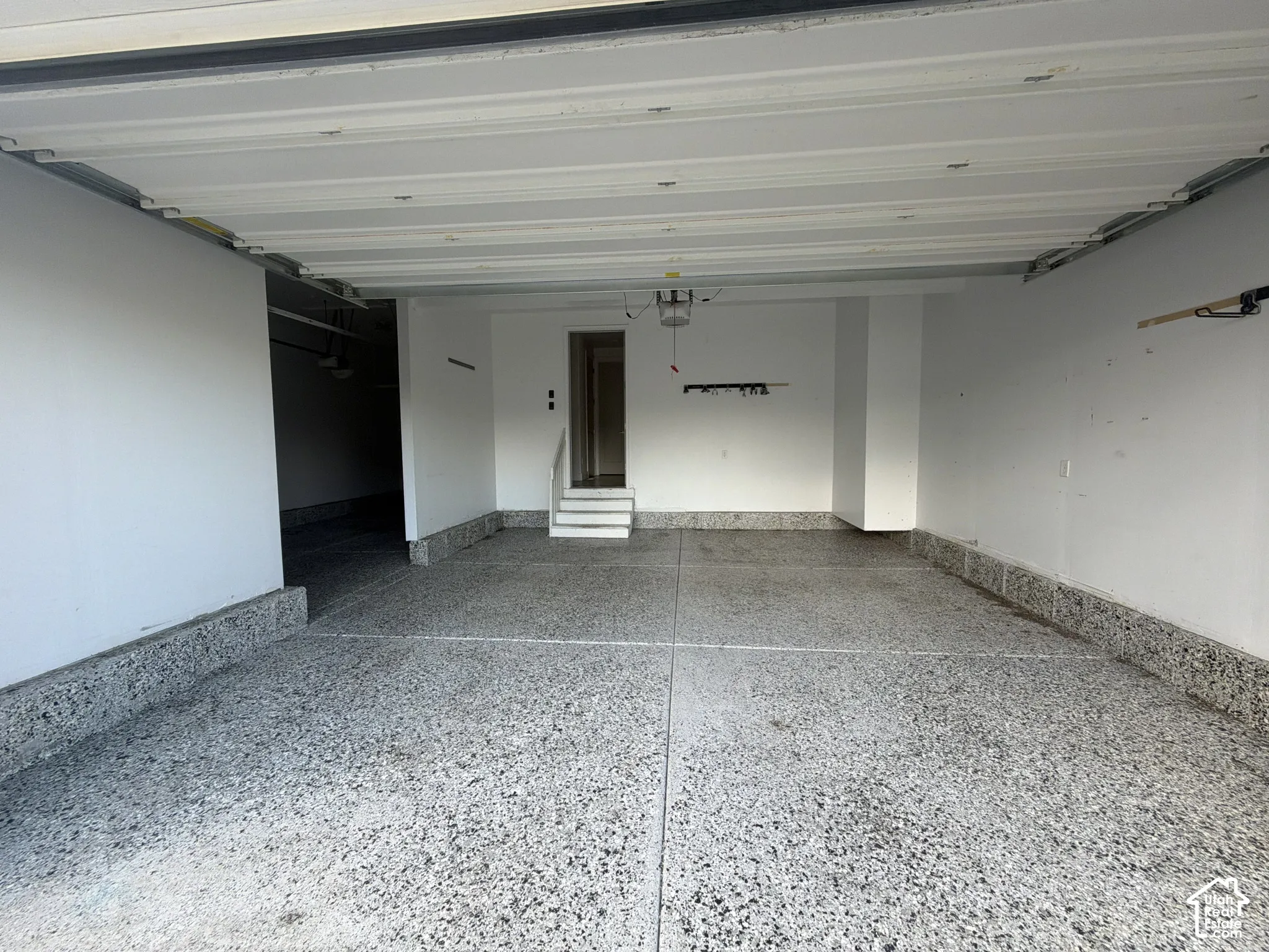 Multi-vehicle garage featuring a speckled epoxy-finish concrete floor, high-clearance overhead door, and concrete stair entry with railing