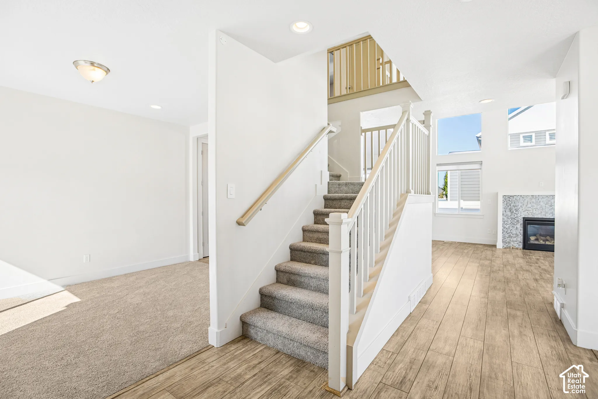 Staircase featuring wood-finish handrails and white balusters, wood-finish flooring, carpeted stairs, recessed lighting, and a fireplace with a textured mosaic surround