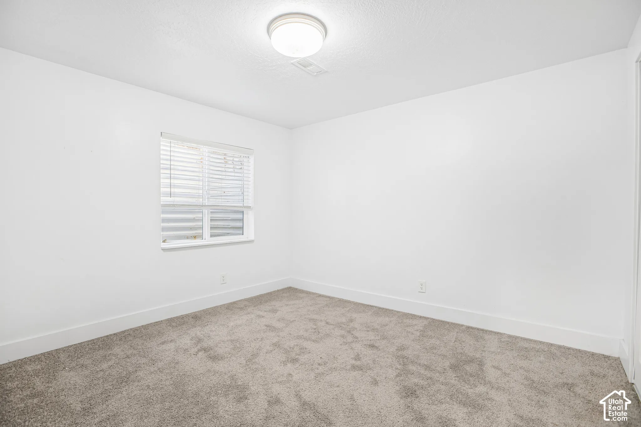 Neutral-toned wall-to-wall carpeting, crisp white walls, and a recessed window featuring horizontal blinds and a flush-mount overhead light fixture