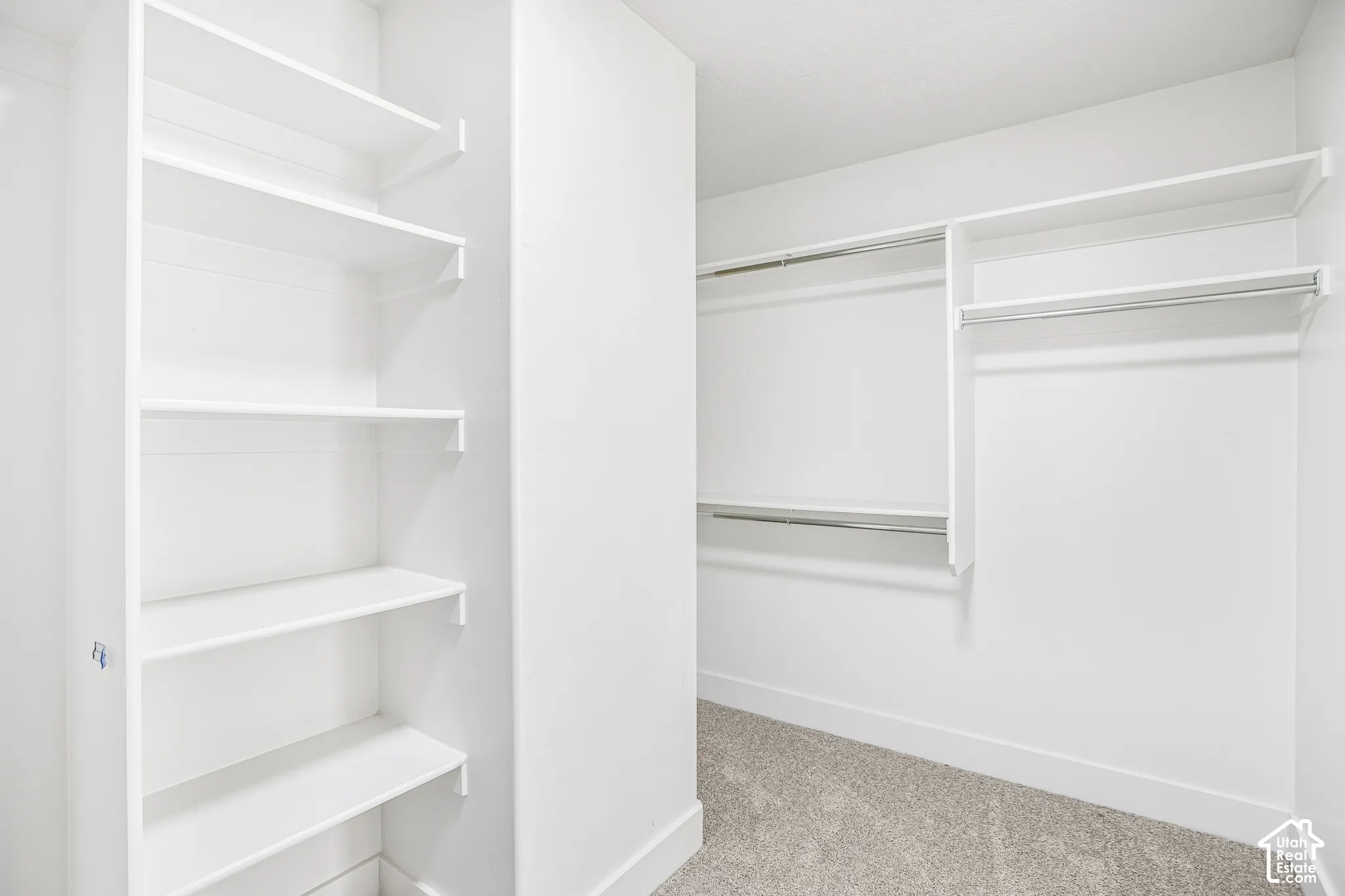 Walk-in storage area featuring custom built-in white shelving, multi-level metal garment rods, and wall-to-wall carpeting