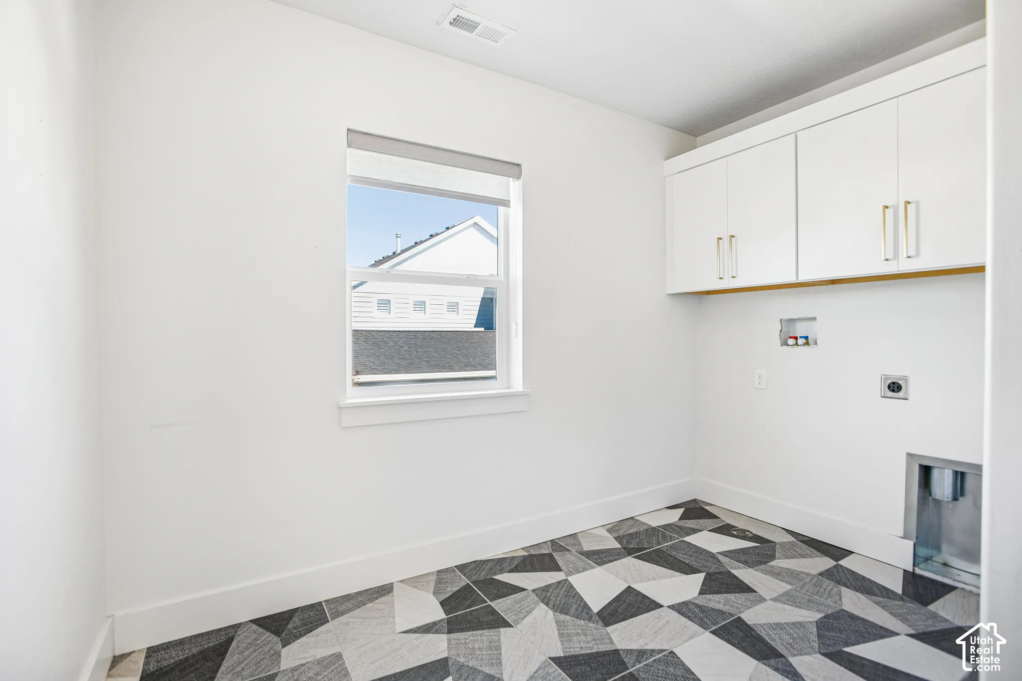 Utility area featuring geometric pattern flooring, white built-in cabinetry with metallic pulls, and a window with a neutral roller shade