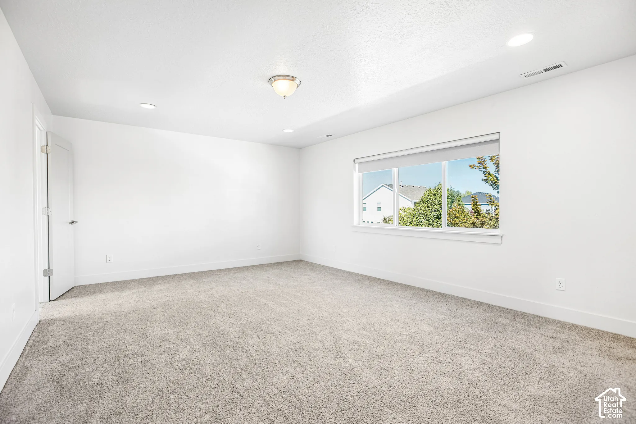 Interior space featuring neutral-toned carpeting, crisp white walls, a large multi-pane window, and recessed ceiling lighting