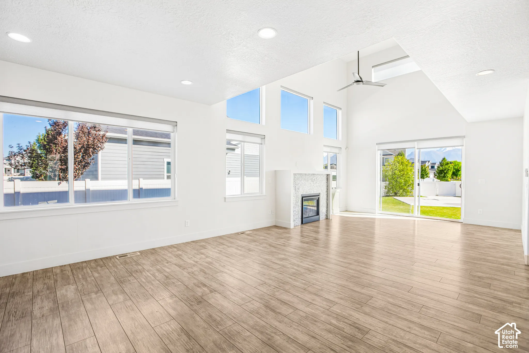 Vaulted ceilings with recessed lighting, tile fireplace surround, wood-finish flooring, and expansive windows