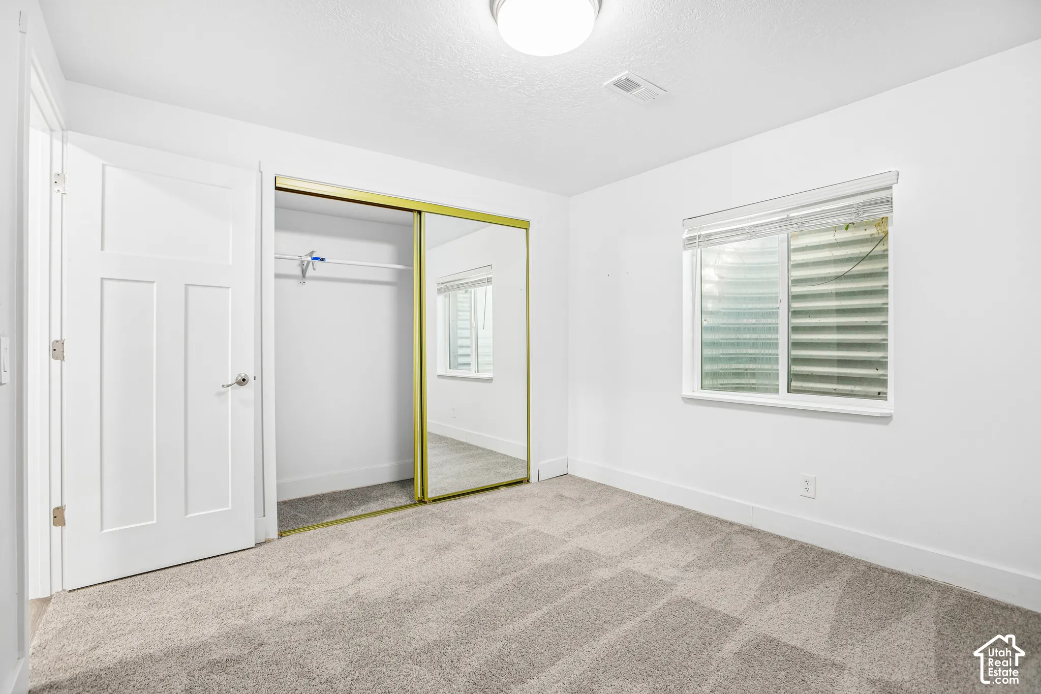 Neutral-toned wall-to-wall carpeting, sliding mirrored closet doors, and a double-hung window with a metal window well
