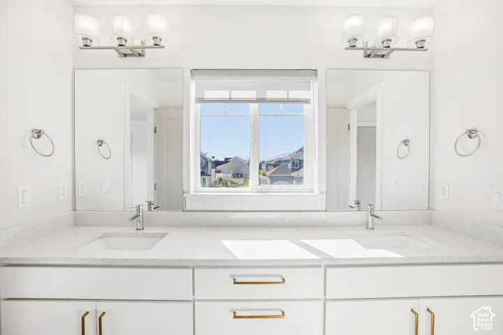 Double vanity featuring white cabinetry, brass-tone hardware, a solid-surface countertop with dual undermount sinks, wall-mounted light fixtures, and two rectangular mirrors