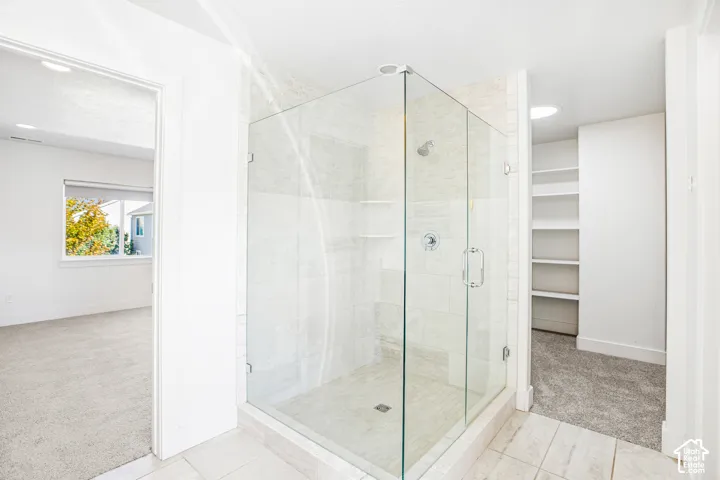 Walk-in shower featuring a glass enclosure, wall-mounted shower head, built-in shelving, and large-format tile wall surrounds, accompanied by built-in shelving units