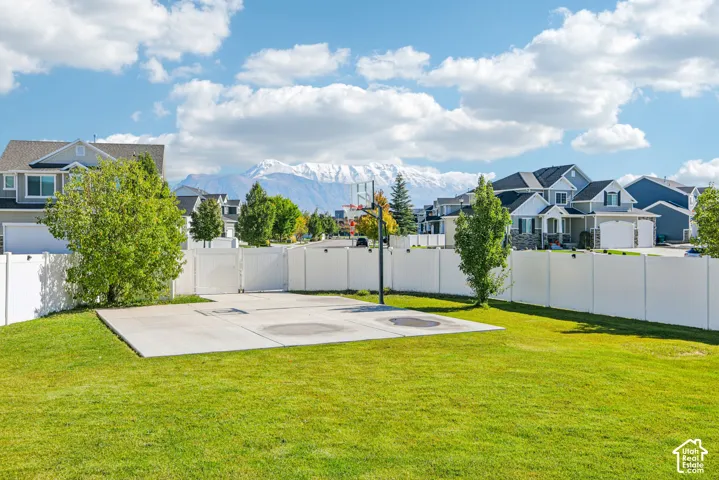 Backyard featuring a concrete sports court, basketball hoop, white vinyl privacy fencing, and mountain backdrop