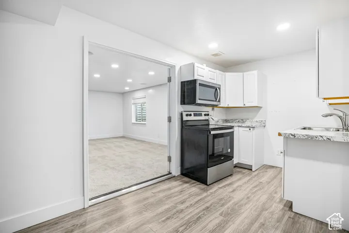 Kitchen featuring white cabinetry, stone-look countertops, stainless steel appliances, and wood-finish flooring, with double-door entry to a carpeted room