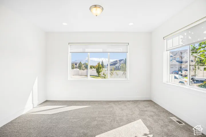 Neutral-toned wall-to-wall carpeting, dual large windows with integrated roller shades, and a mountain backdrop