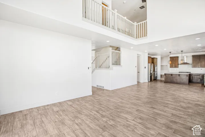 Two-story foyer featuring wood-finish flooring, a white vertical balustrade, recessed lighting, and a kitchen equipped with dark wood-finish cabinetry and a central island