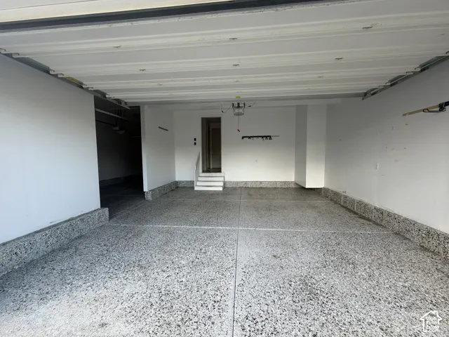 Multi-vehicle garage featuring a speckled epoxy-finish concrete floor, high-clearance overhead door, and concrete stair entry with railing