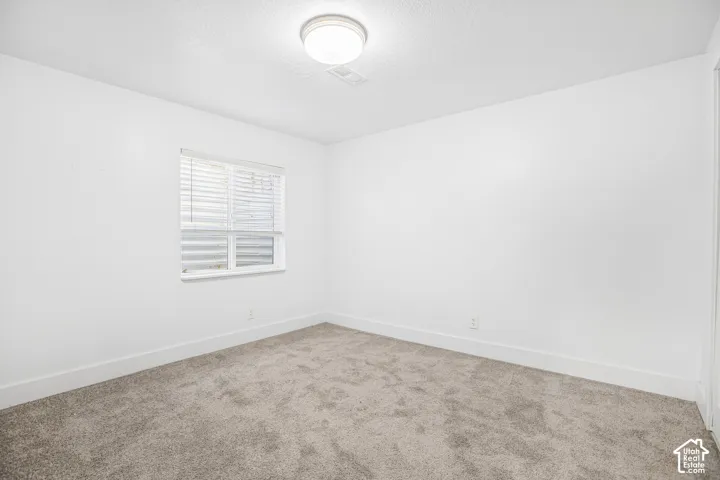 Neutral-toned wall-to-wall carpeting, crisp white walls, and a recessed window featuring horizontal blinds and a flush-mount overhead light fixture