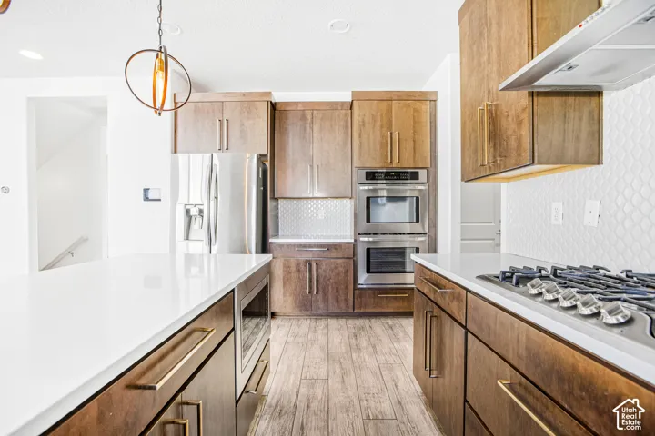Kitchen featuring medium-tone wood cabinetry, white quartz countertops, stainless steel double wall ovens, a gas cooktop, and wood-finish flooring