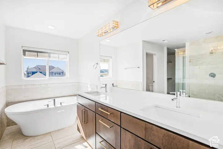 Double vanity with quartz countertops and undermount sinks, wood-finish cabinetry, freestanding soaking tub, and walk-in shower with tile surround