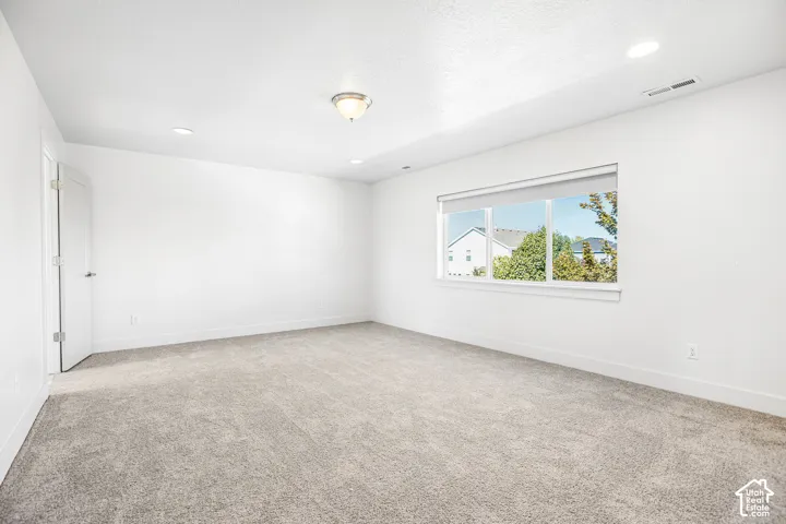 Interior space featuring neutral-toned carpeting, crisp white walls, a large multi-pane window, and recessed ceiling lighting